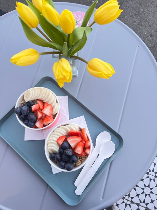 Free Top view of vibrant fruit bowls with bananas, strawberries, and blueberries beside yellow tulips. Stock Photo