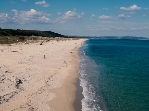 Free Aerial view of a tranquil sandy beach stretching along the clear turquoise sea under a blue sky. Stock Photo