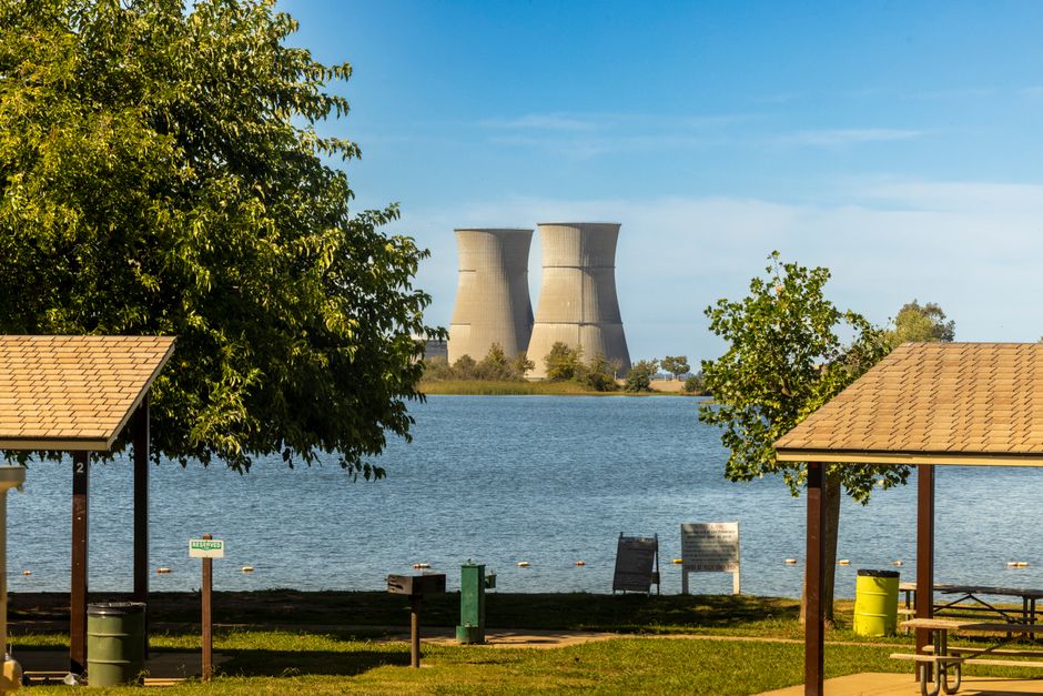 Cooling towers visible from a park by the lake during a sunny day with clear skies.