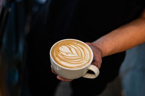 Free Close-up of a barista's hand holding a latte featuring intricate latte art. Stock Photo