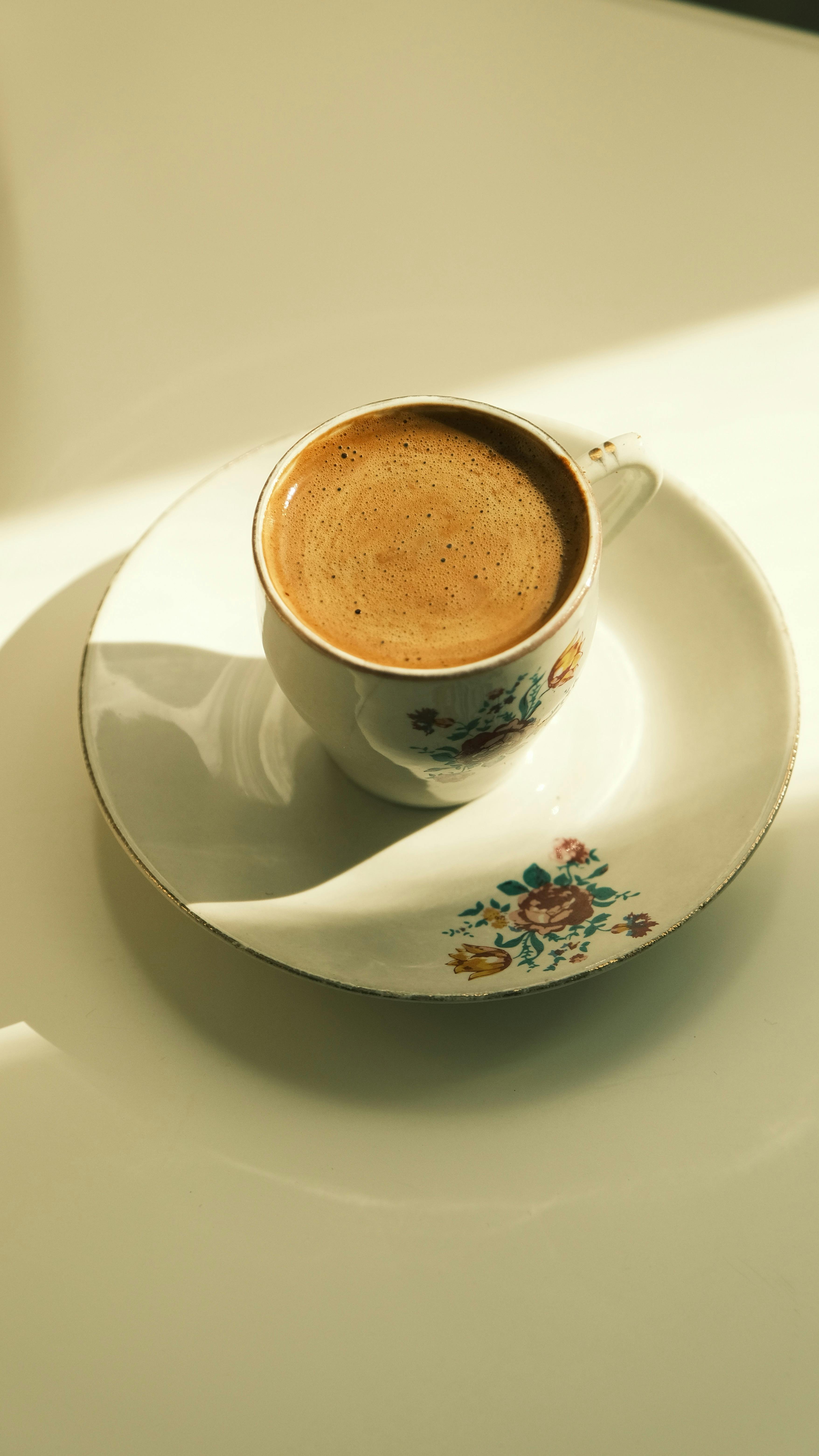 A beautifully decorated floral teacup filled with hot espresso, casting a warm shadow.
