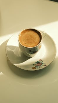 A beautifully decorated floral teacup filled with hot espresso, casting a warm shadow.