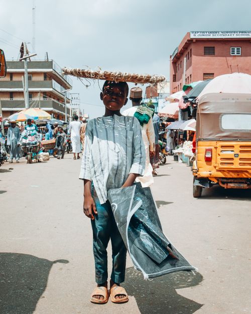 Free A young boy amidst the bustling market in Kaduna, balancing goods on his head, capturing local life. Stock Photo