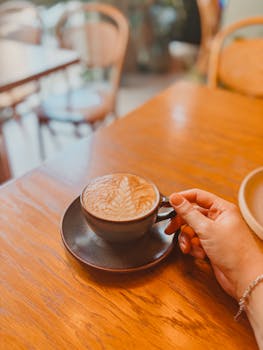 Warm latte with latte art held by a hand in a comforting cafe setting.