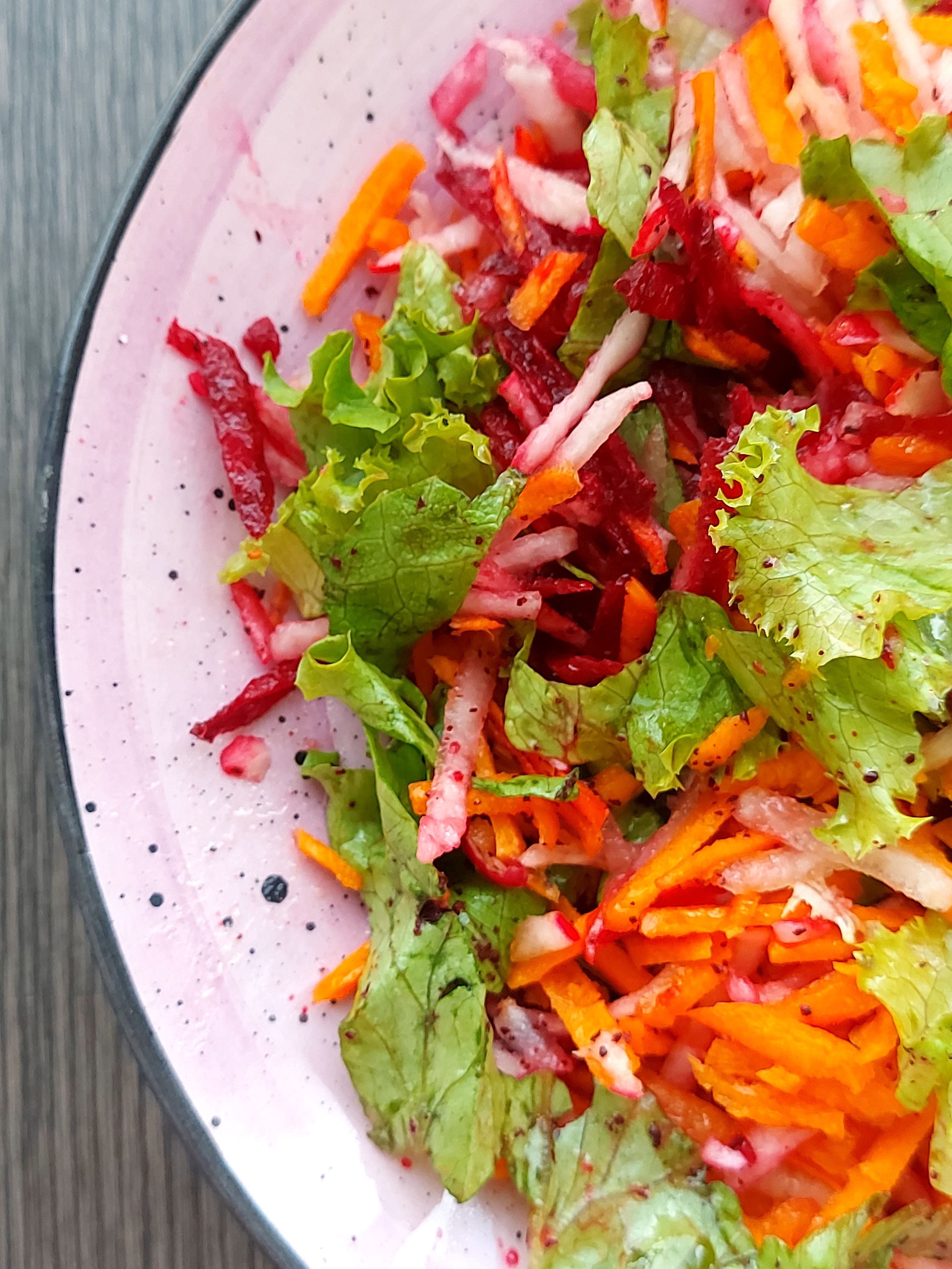 Colorful fresh vegetable salad with lettuce, beetroot, and carrots in a pink bowl.