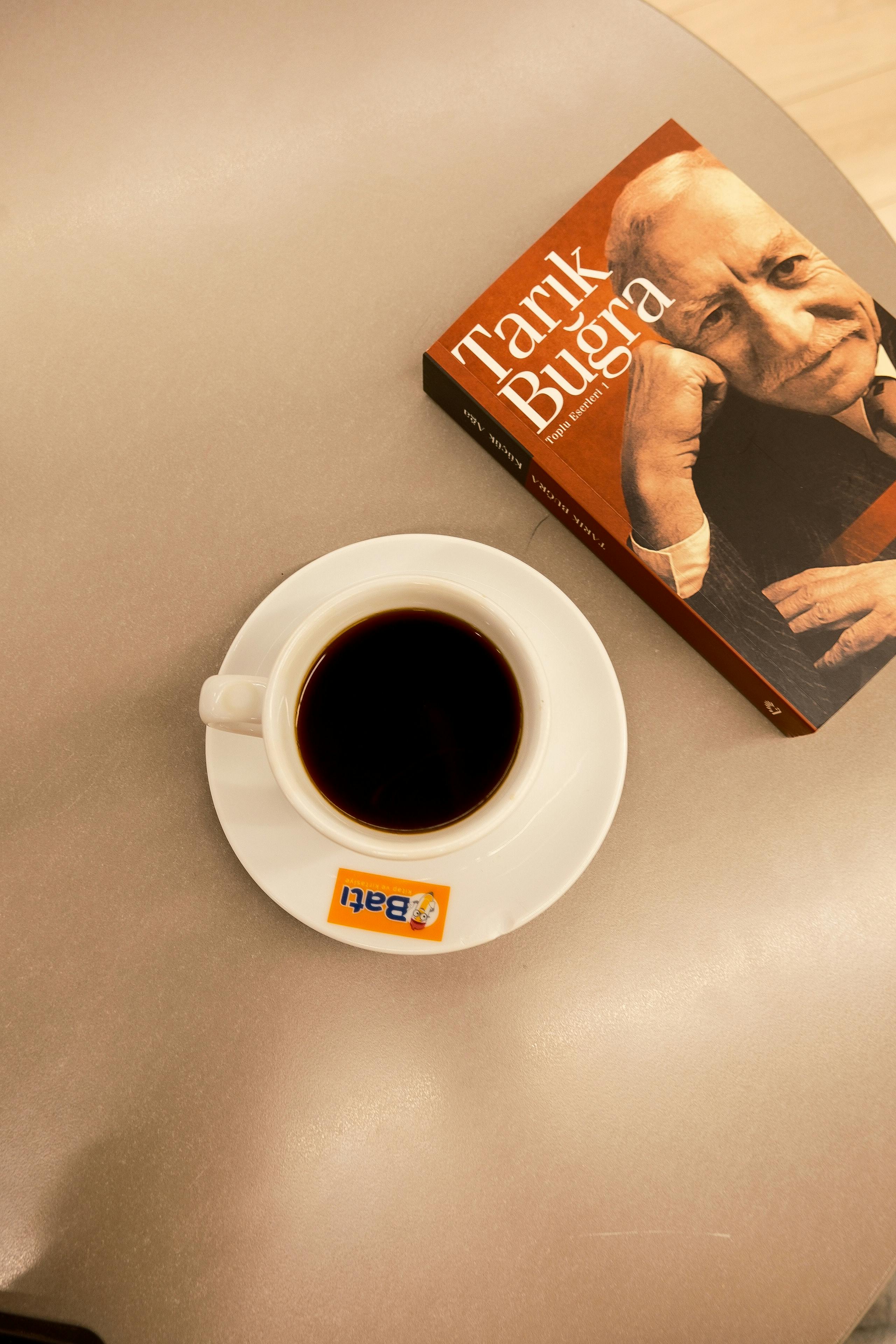 A cup of black coffee next to a book on a beige table, cozy setup.