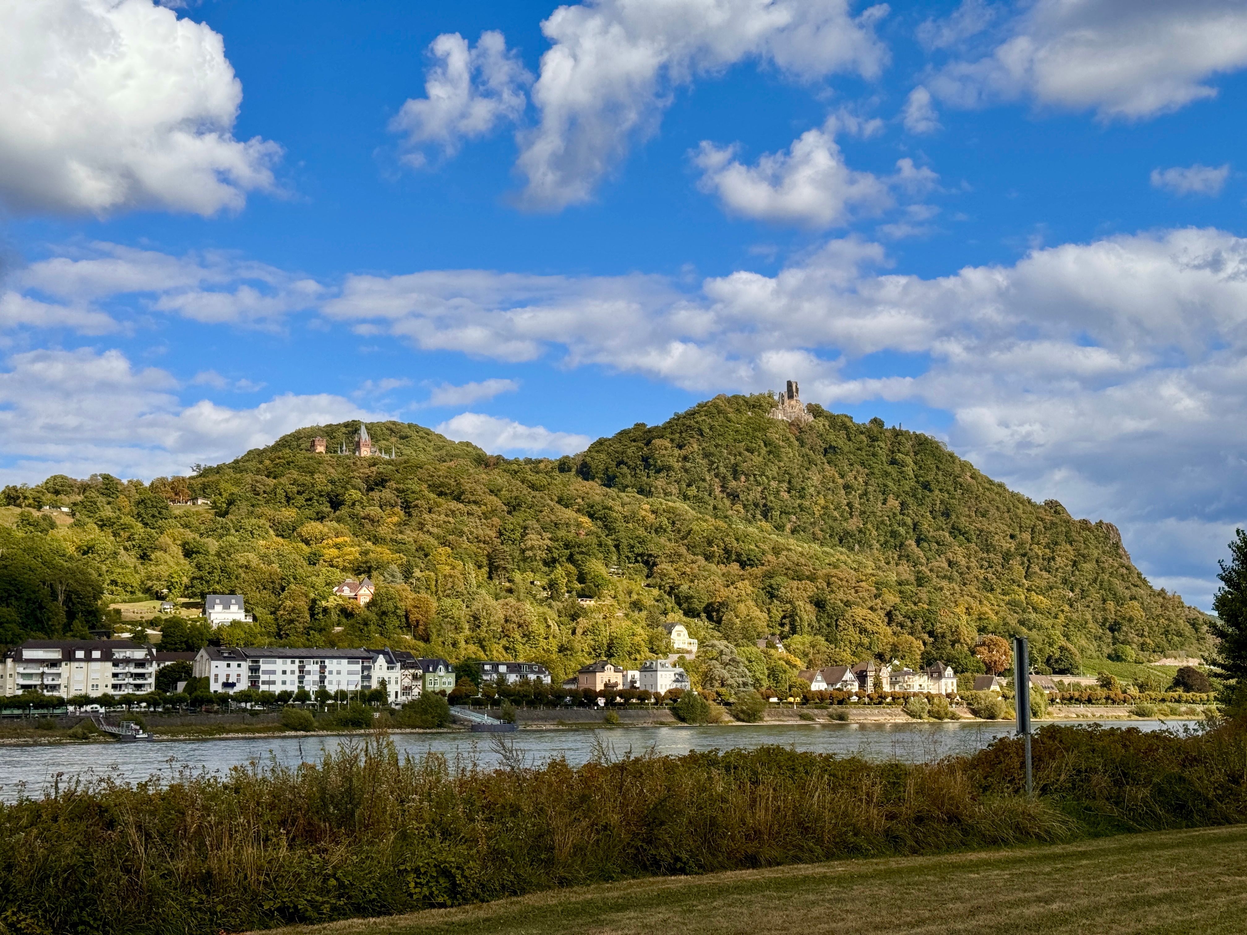 Radfahrer entlang des malerischen Rheinufers mit historischen Burgen im Hintergrund