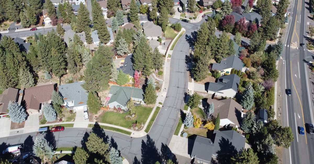 Aerial view of a tree-lined suburban neighborhood with houses and curved streets on a sunny day.