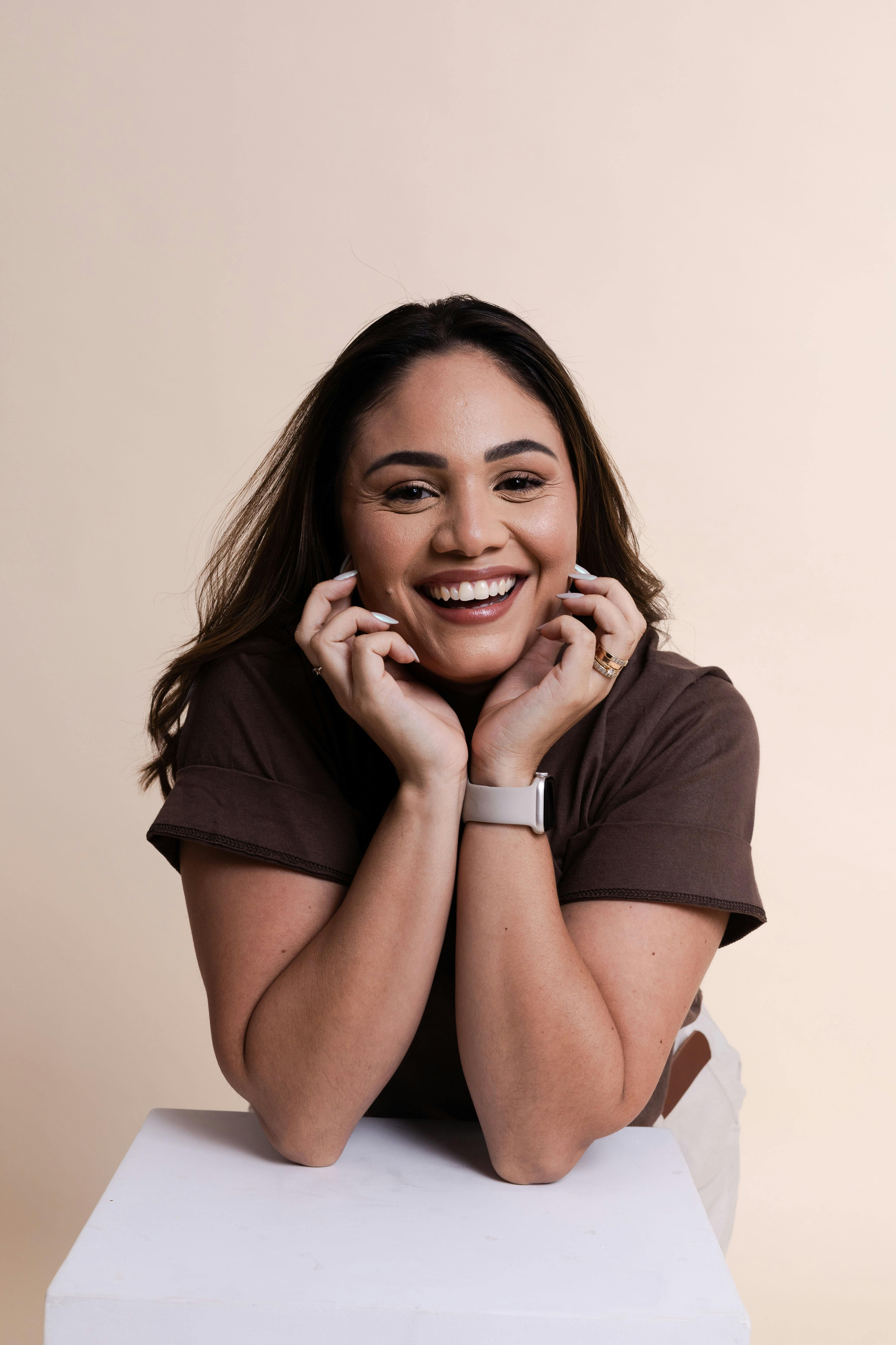 Cheerful woman posing with hands on chin in a friendly studio portrait.