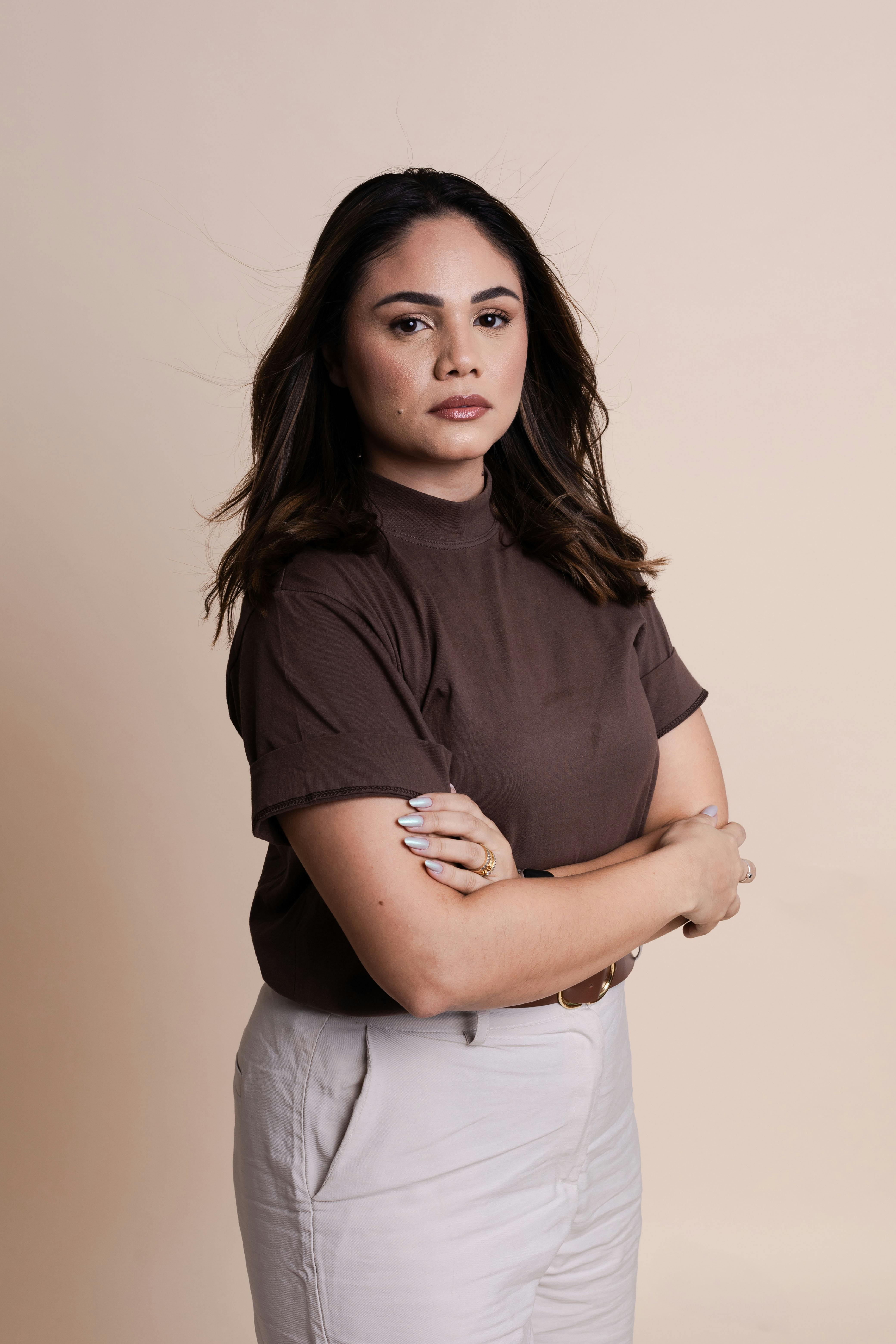 Portrait of a confident woman in a studio setting, arms crossed, with a neutral background.