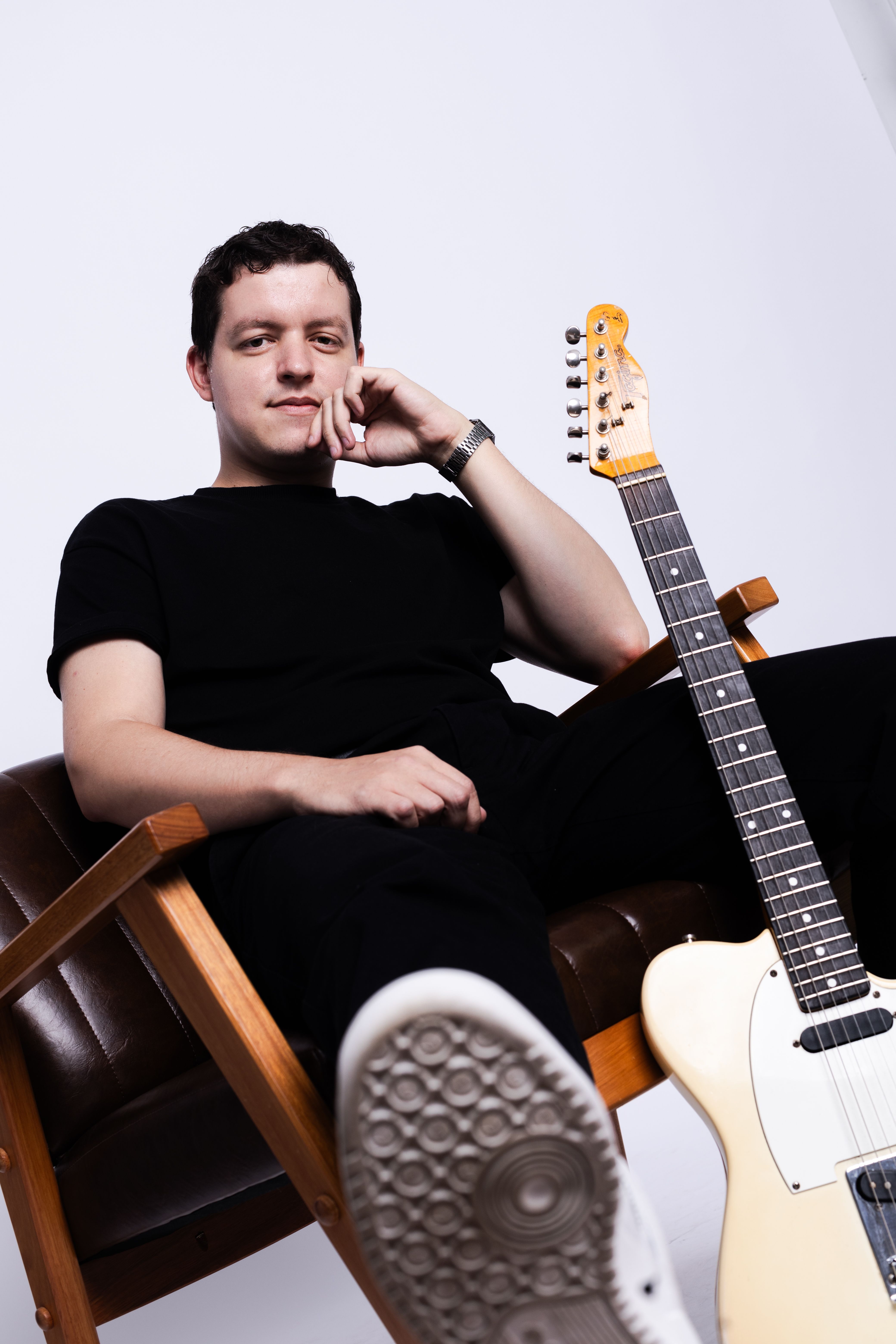 Man sitting casually with an electric guitar beside him, exuding a relaxed and creative vibe.