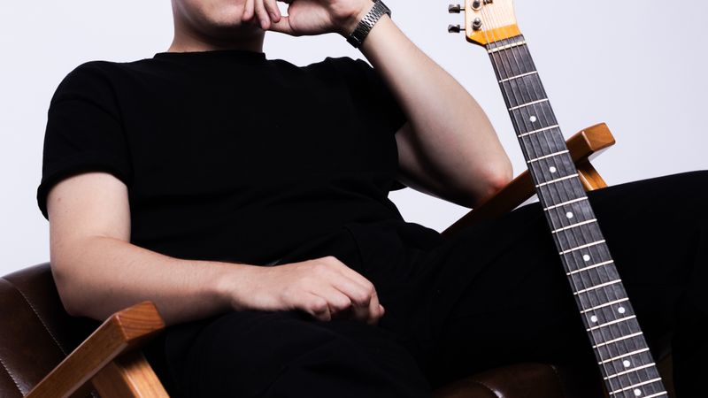 Man sitting casually with an electric guitar beside him, exuding a relaxed and creative vibe.