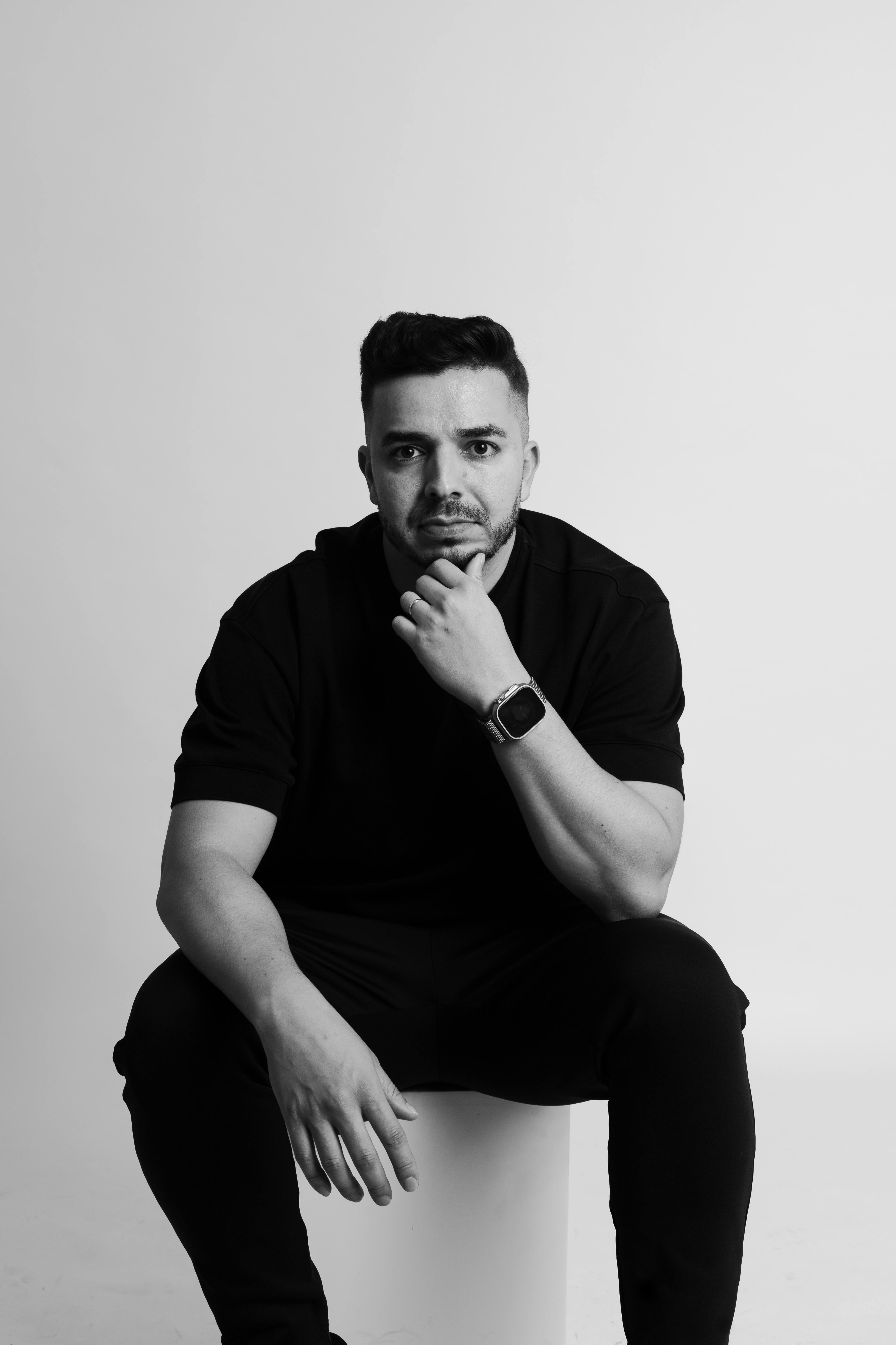 Monochrome portrait of a man seated with a thoughtful expression wearing a smartwatch.