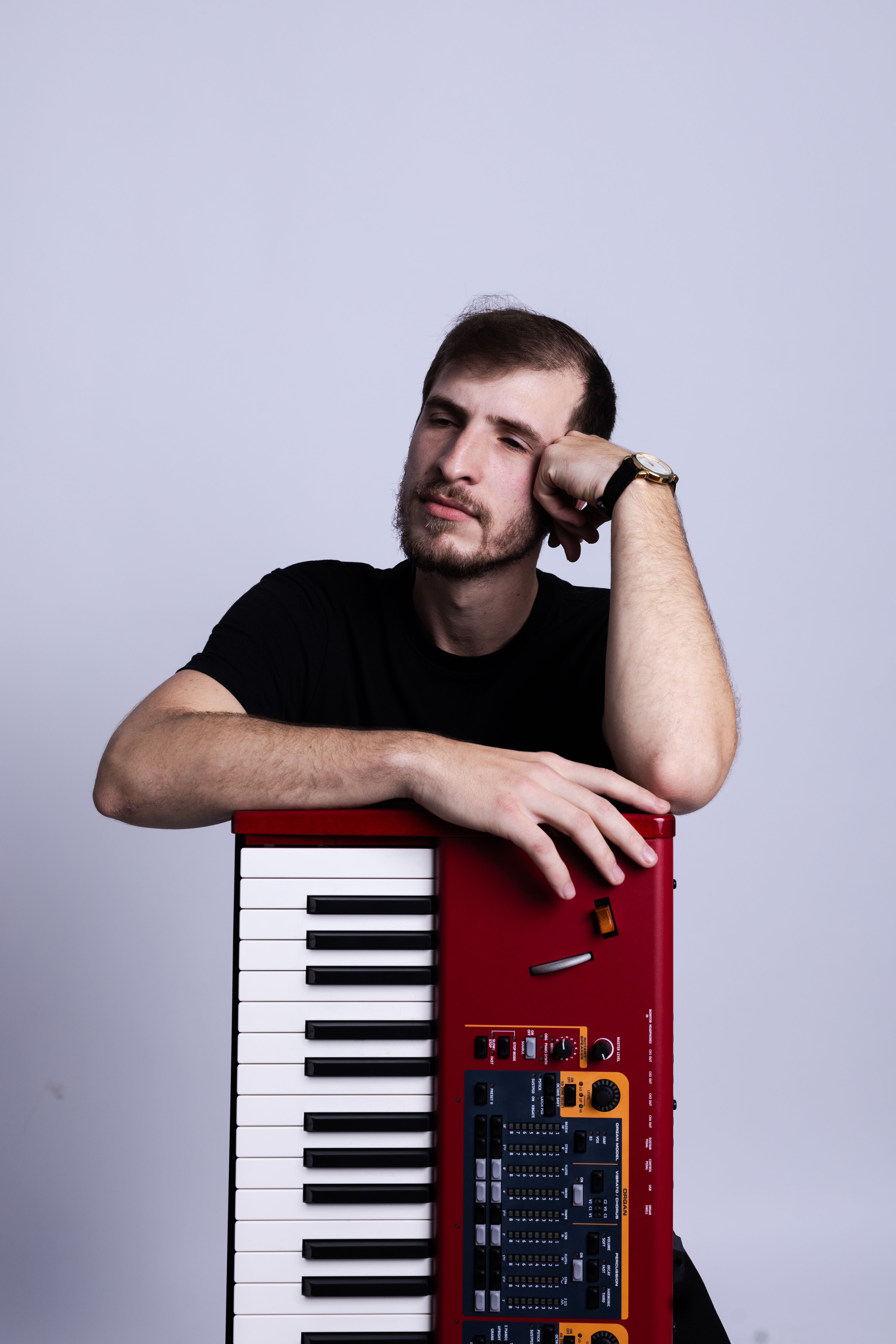 Young male musician leaning on a red electronic keyboard with a thoughtful expression.