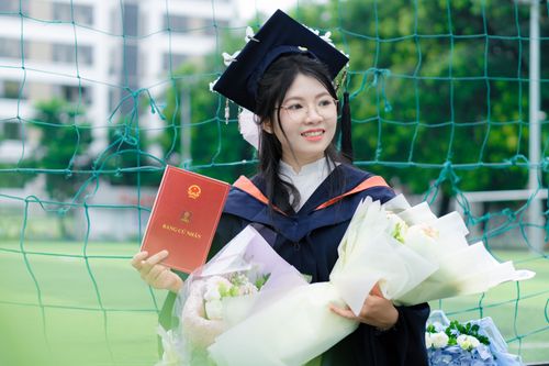 Free Happy graduate in cap and gown holding diploma and bouquets celebrating outdoors. Stock Photo