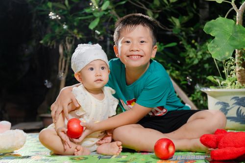 Free Two joyful siblings enjoying playtime with red apples and toys outdoors in natural light. Stock Photo