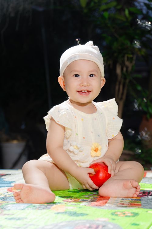 Free Smiling baby in white clothing holds a red toy ball, adding charm and joy. Stock Photo