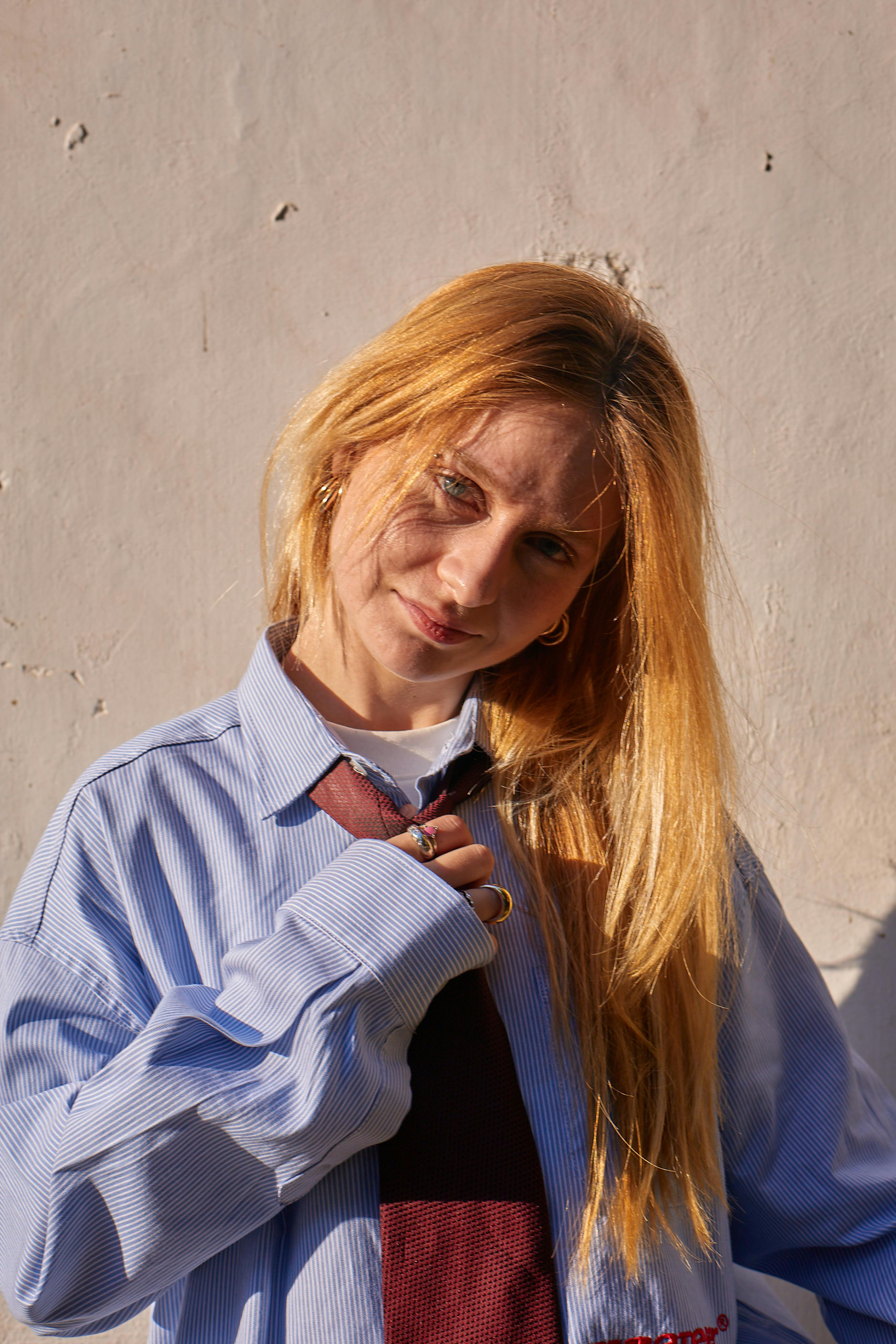 grátis Retrato de uma jovem mulher em pose relaxada, vestindo camisa e gravata, aproveitando a luz quente do sol. Foto profissional