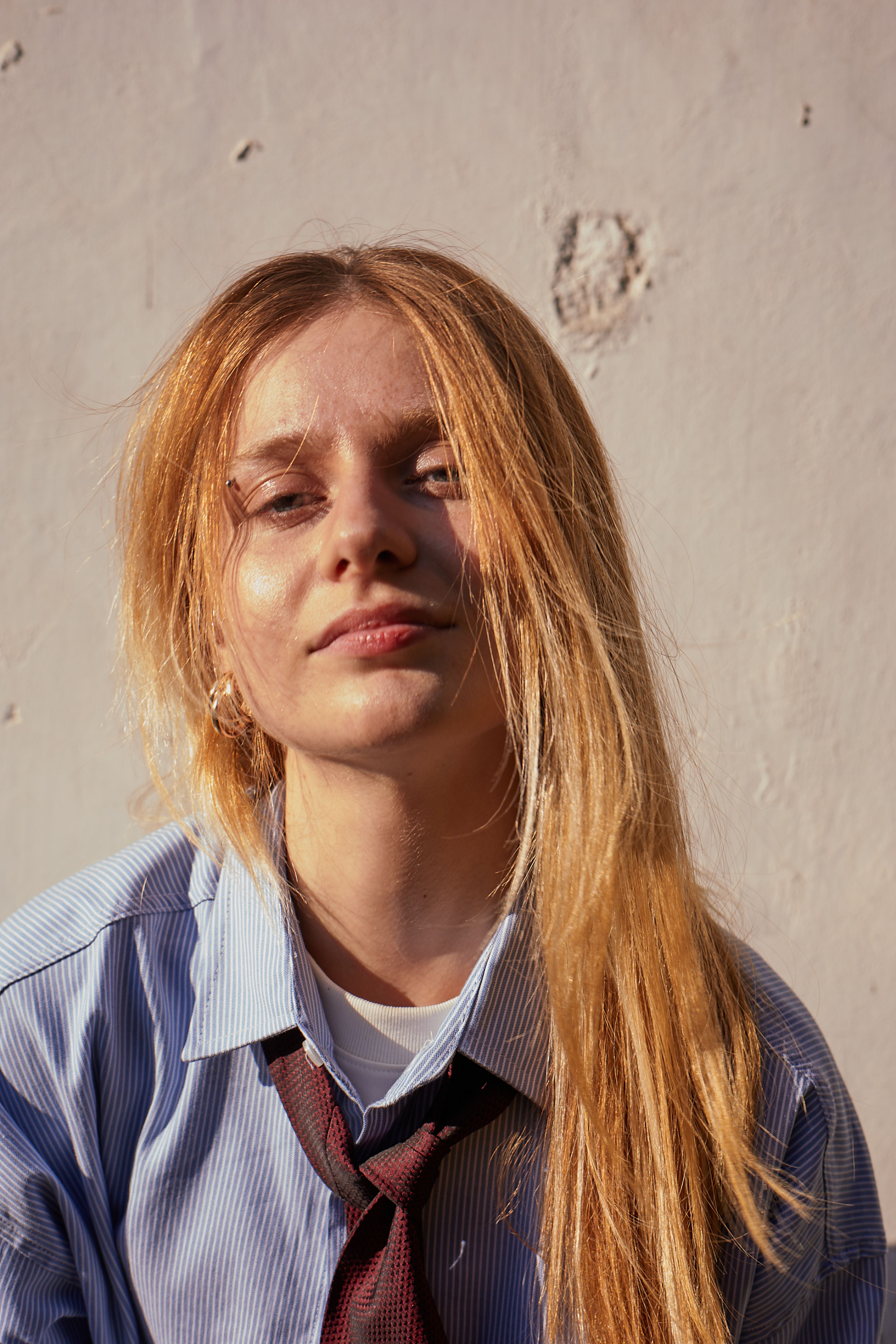 Portrait of a young woman in casual attire enjoying sunlight against a textured wall.