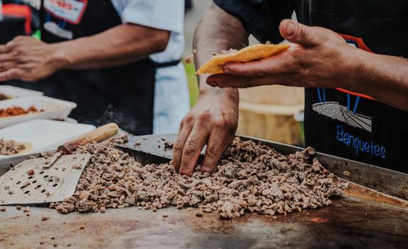 Close-up of a vendor preparing delicious tacos on a hot griddle at an outdoor street food market.