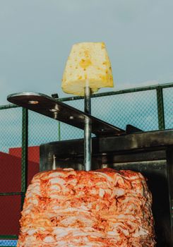 Juicy al pastor meat with a slice of pineapple on a vertical rotisserie outdoors.
