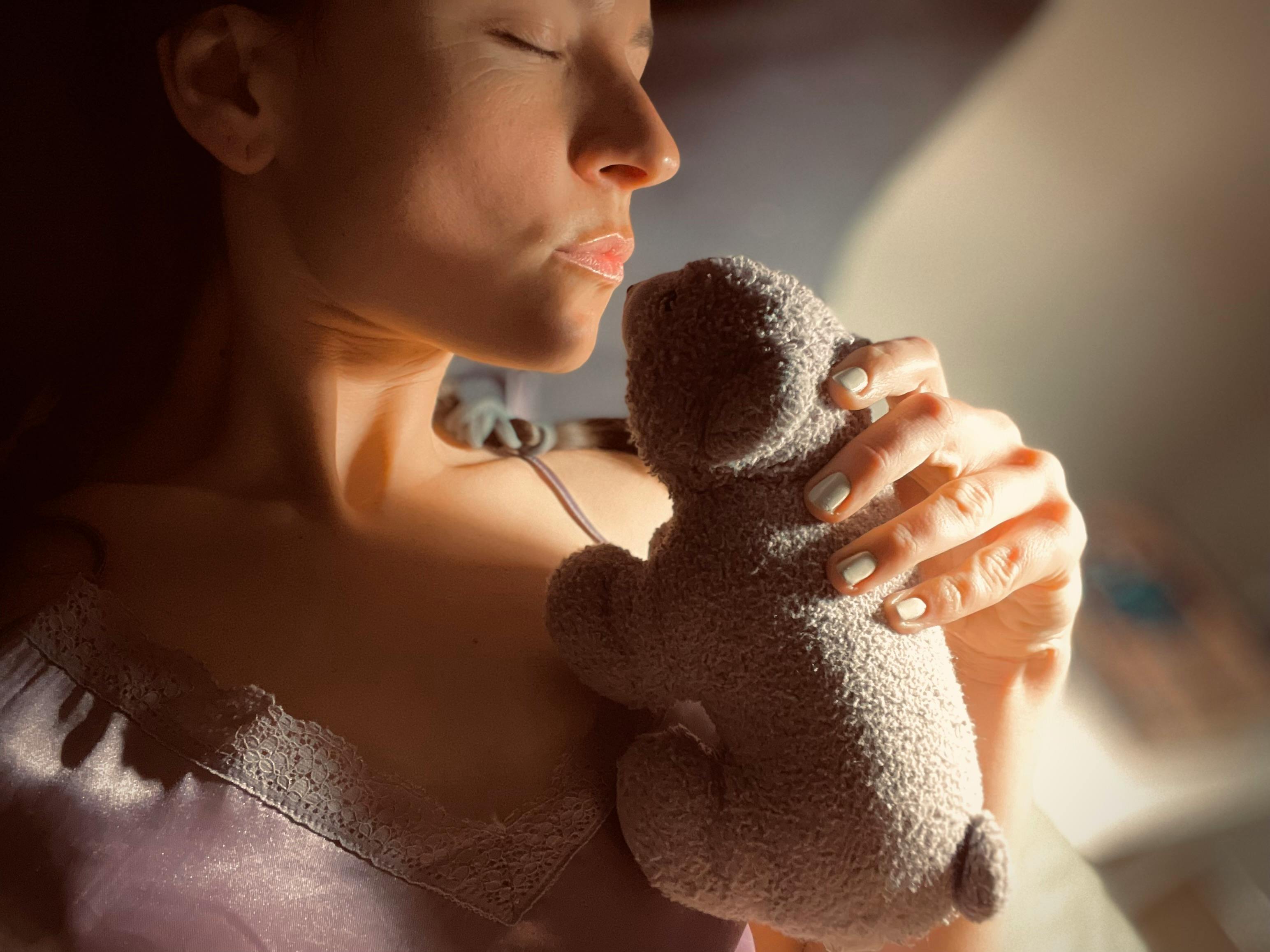 A young woman peacefully resting with a teddy bear, bathed in warm light.