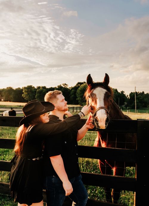 Free A couple interacts with a horse at a countryside ranch during sunset. Stock Photo