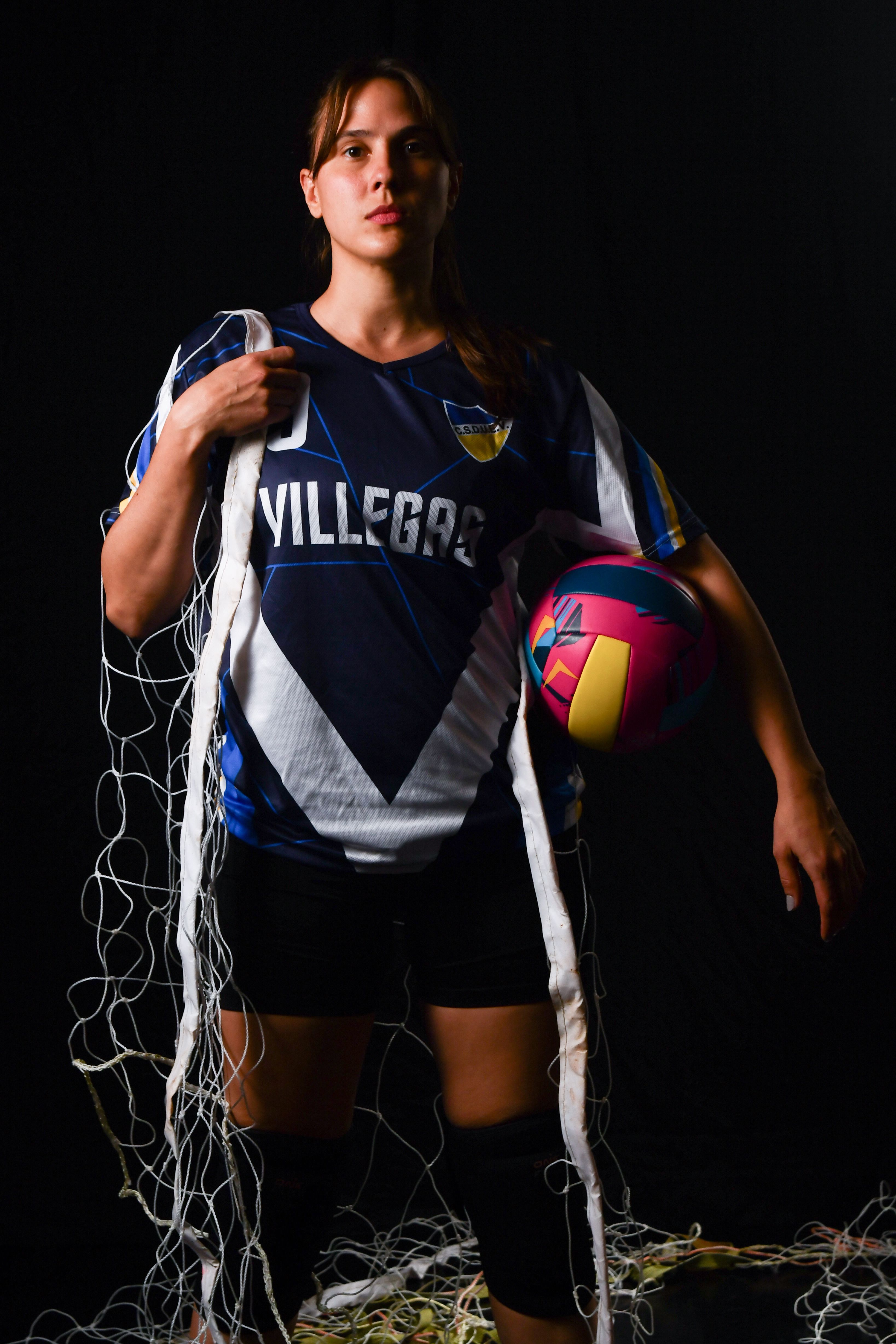 Strong female volleyball player posing with ball and net on dark background.