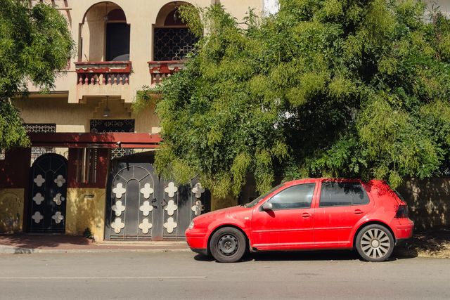 Red hatchback parked in the shade of a street tree — photo by Hassan Bouamoud on Pexels