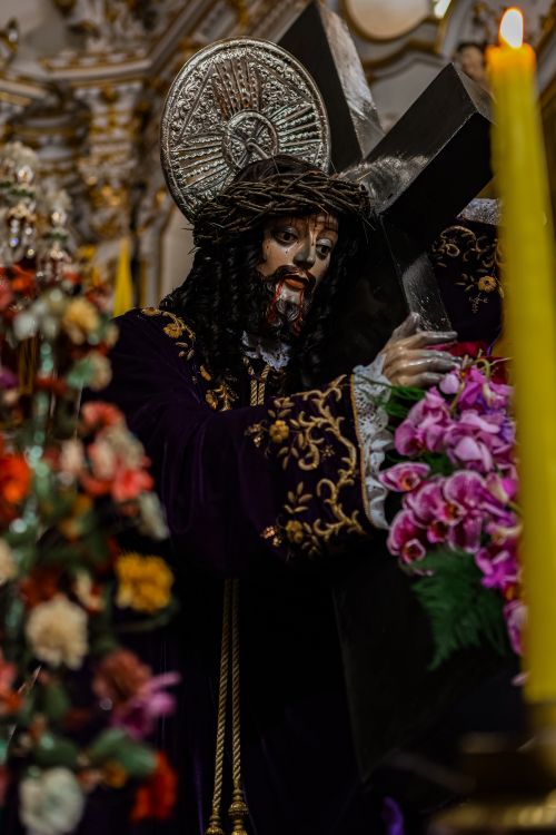 Free Intricate religious statue carrying a cross surrounded by vibrant flowers in an ornate setting. Stock Photo