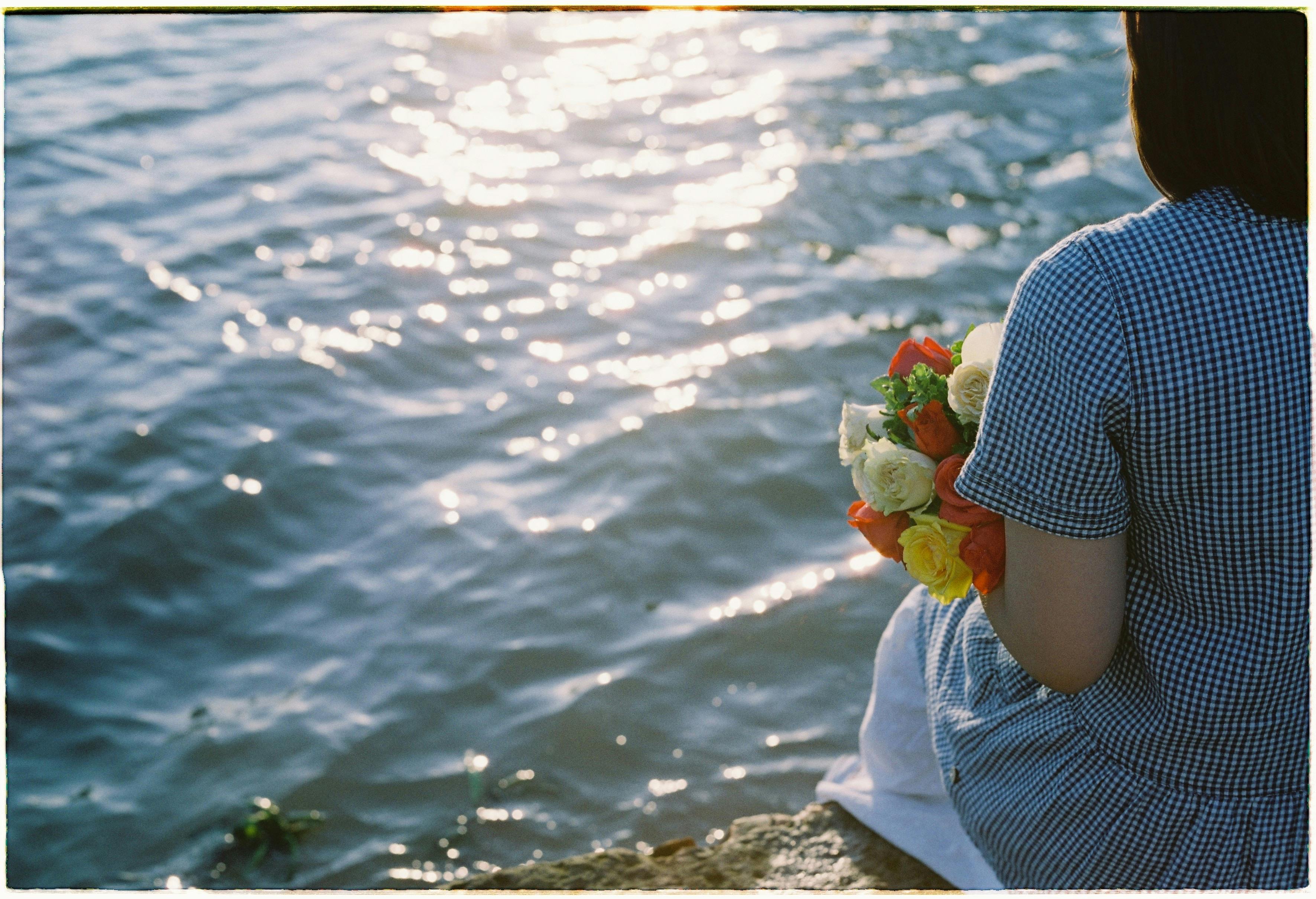 A serene moment by the water as a woman holds a colorful bouquet in her hands.