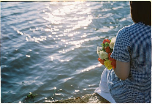A serene moment by the water as a woman holds a colorful bouquet in her hands.