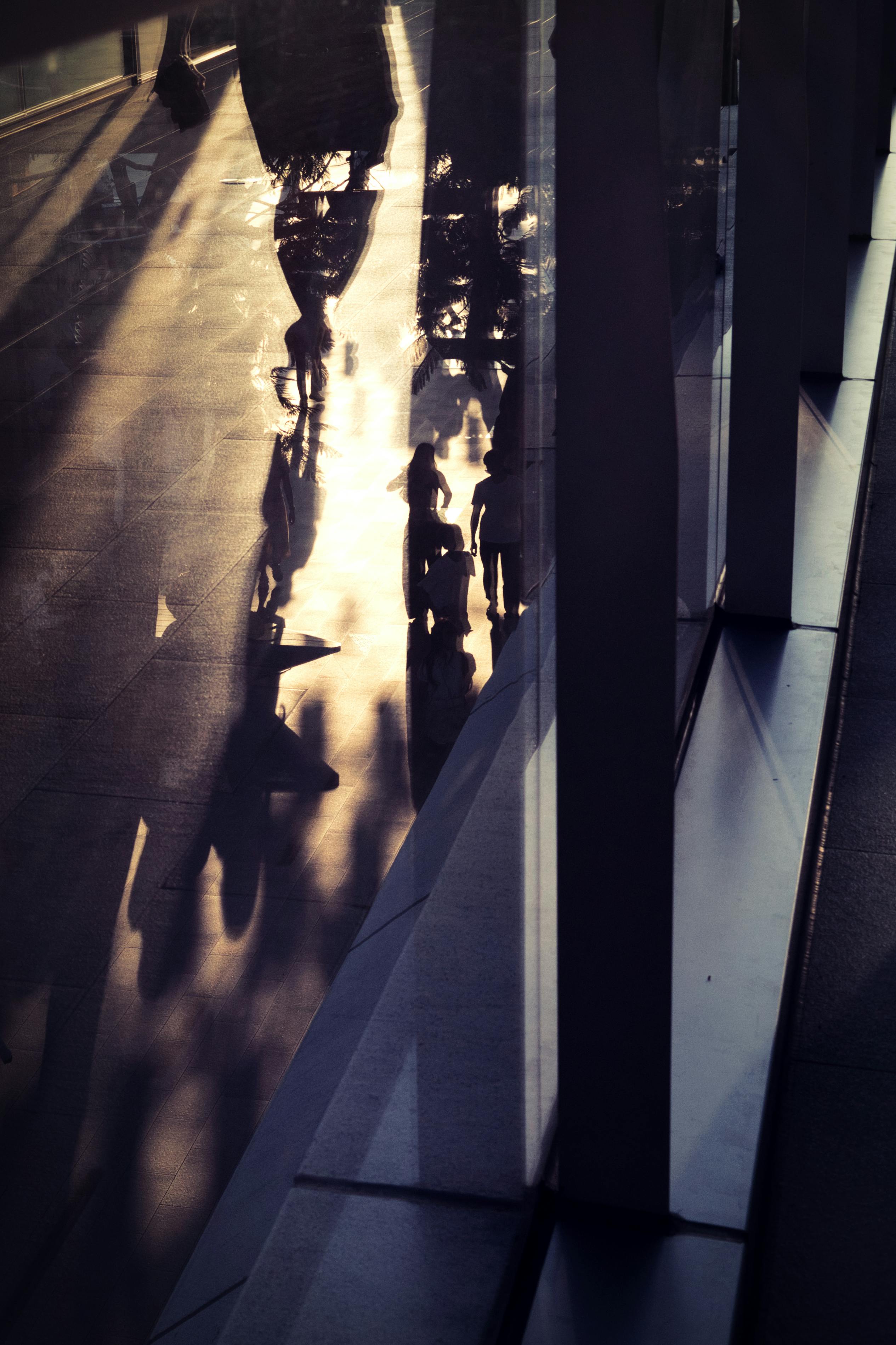 Gratuit Des silhouettes sombres se projettent sur un trottoir de la ville au crépuscule, créant une scène urbaine abstraite. Photos