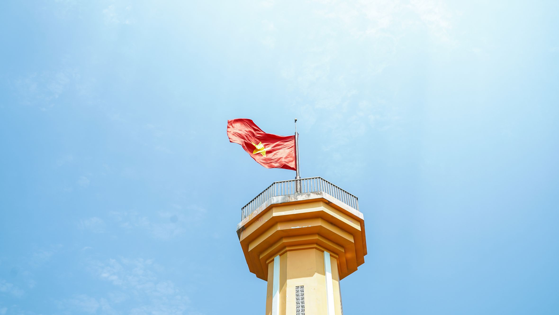 Vietnamese flag waving atop a monument tower under a clear blue sky on Ly Son Island.