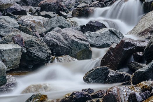 A tranquil stream cascades over rocks in a serene natural setting, captured with a long exposure.