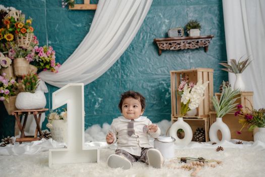Adorable baby boy celebrating first birthday with floral decorations indoors.