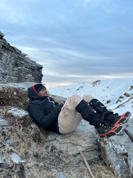 Man rests on snowy mountainside during winter hike, capturing nature's tranquility.