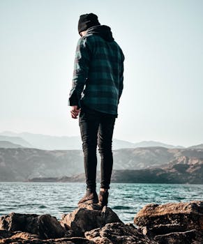 一个男人穿着休闲服装，站在湖边宁静的岩石上，欣赏着户外景色