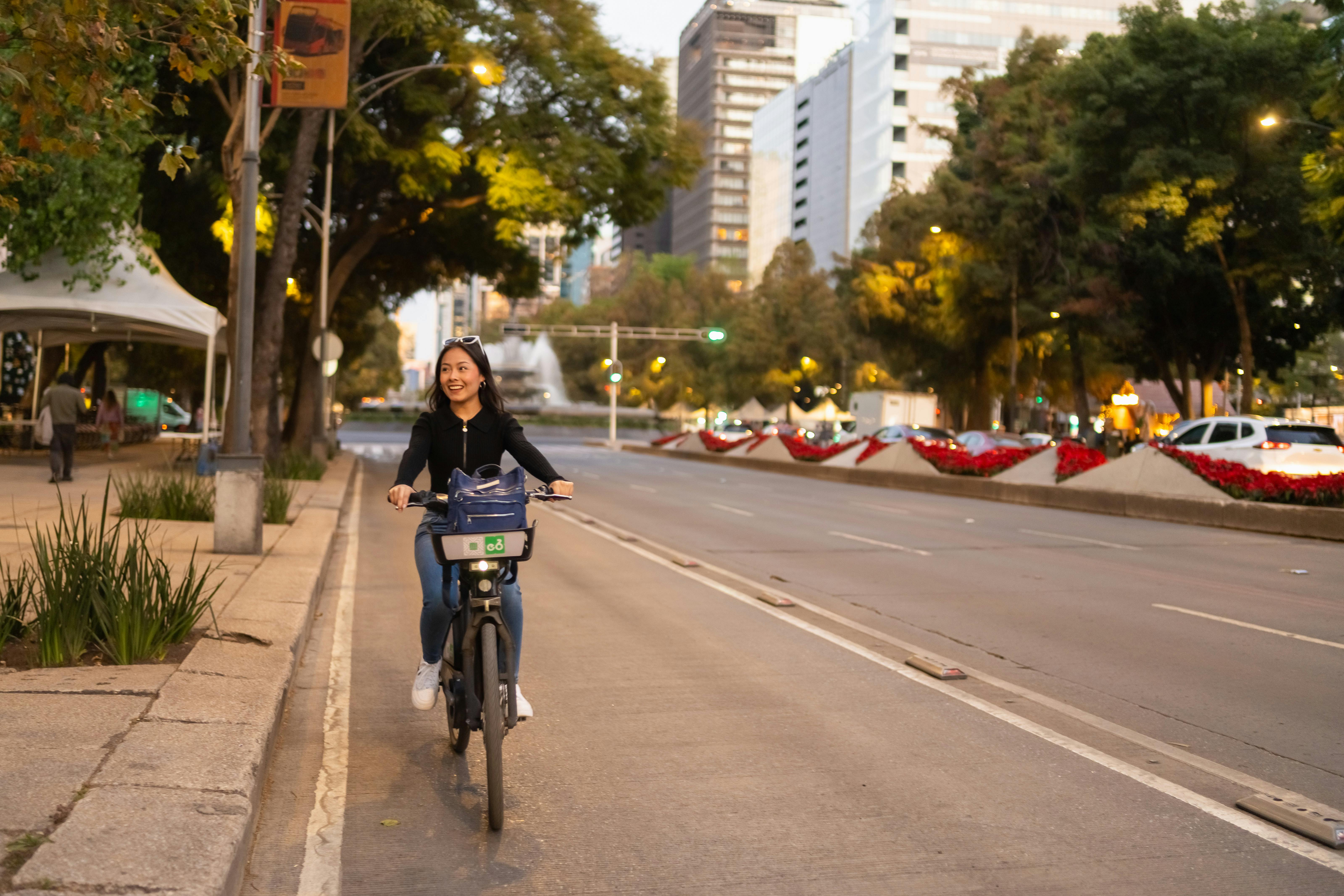 A woman enjoys a bike ride on a vibrant city street during the early evening in Mexico City.