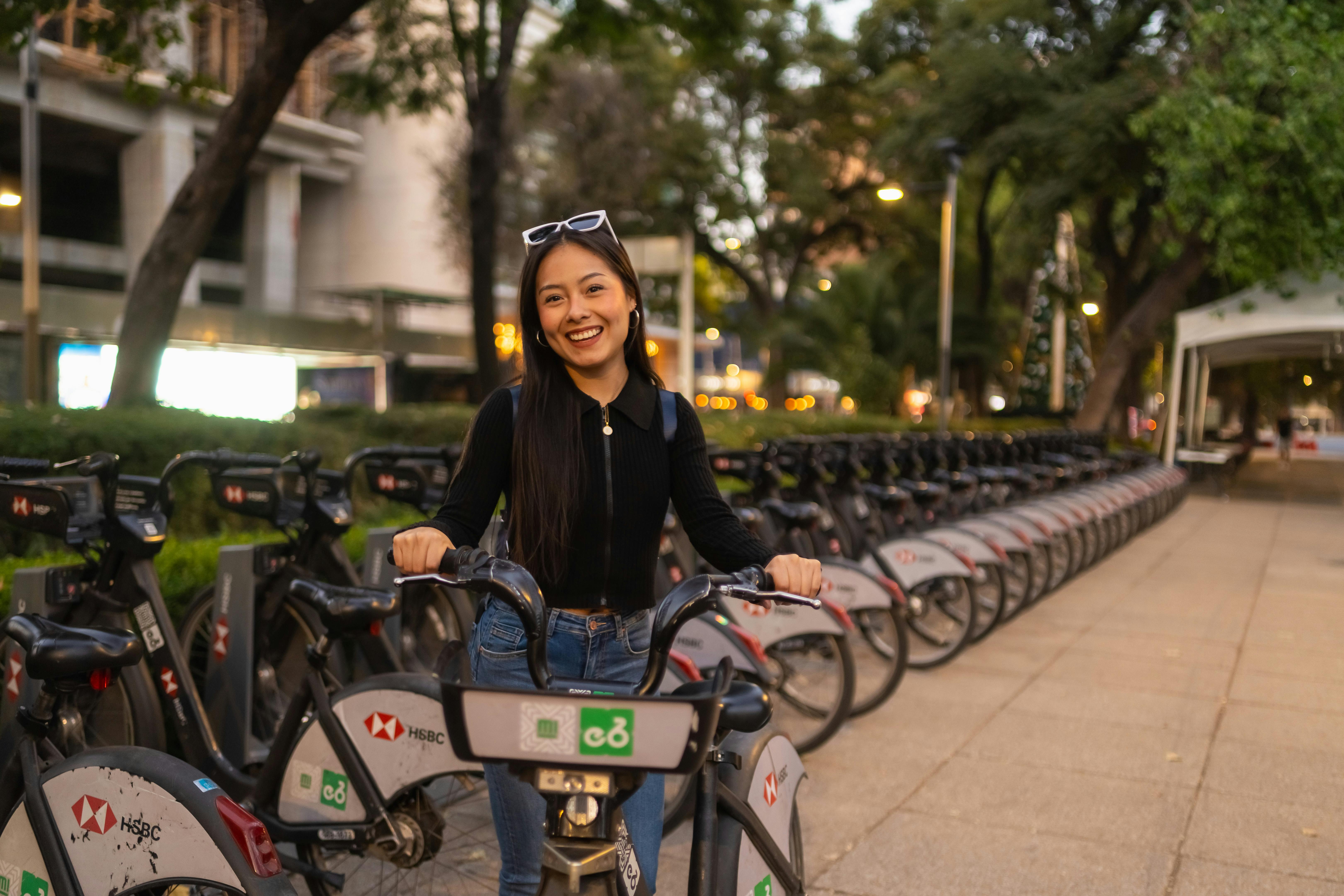Young woman smiling while posing with rental bike in a park in Mexico City at dusk.