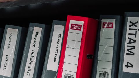 Color-coded office binders organized neatly in a storage shelf, featuring labels and a striking red binder.