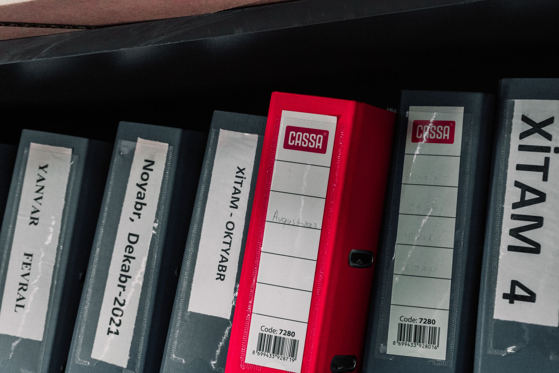 Color-coded office binders organized neatly in a storage shelf, featuring labels and a striking red