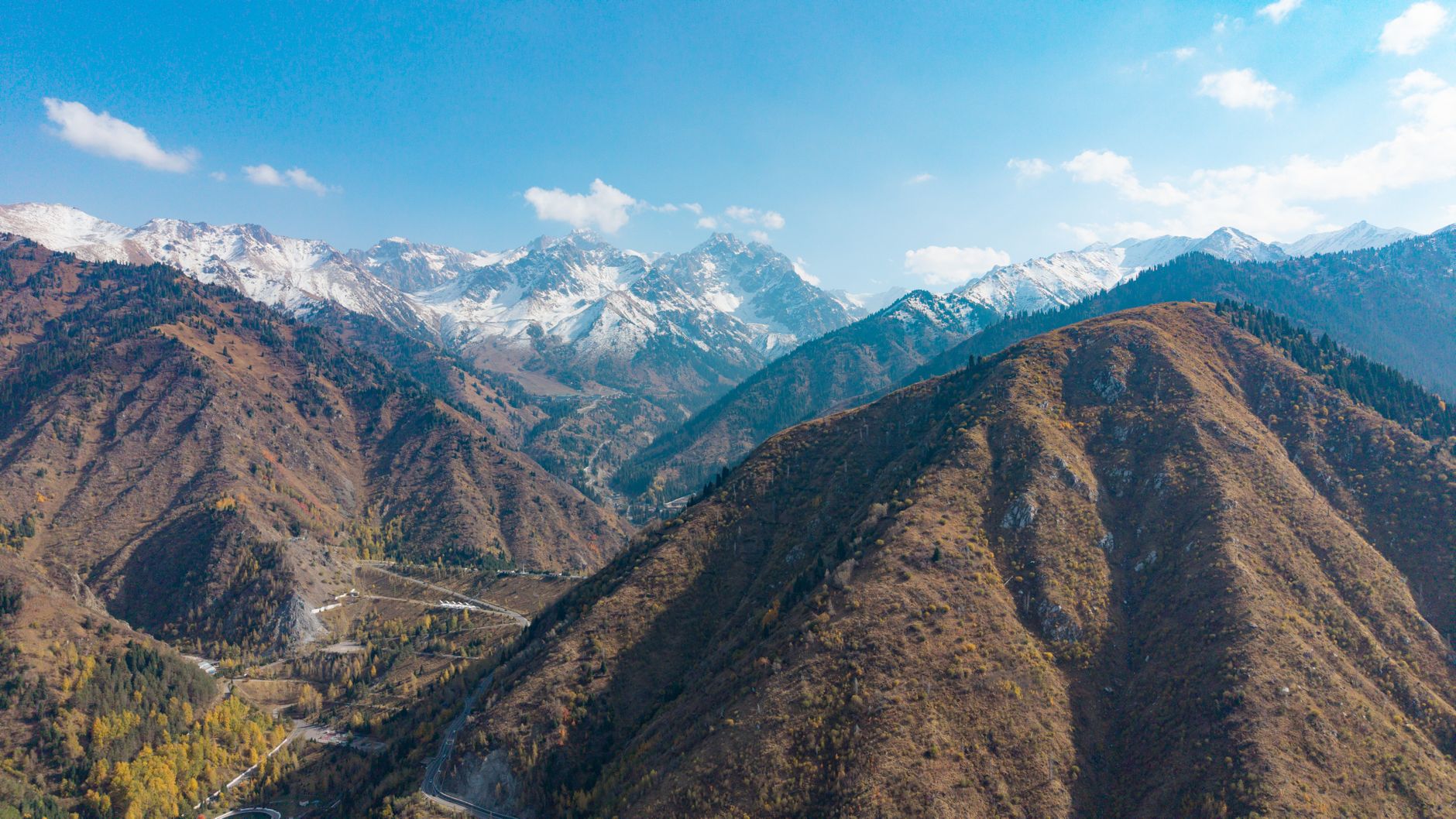 Stunning aerial view of the Tian Shan mountain range in Kazakhstan showcasing snow-capped peaks and autumn foliage.