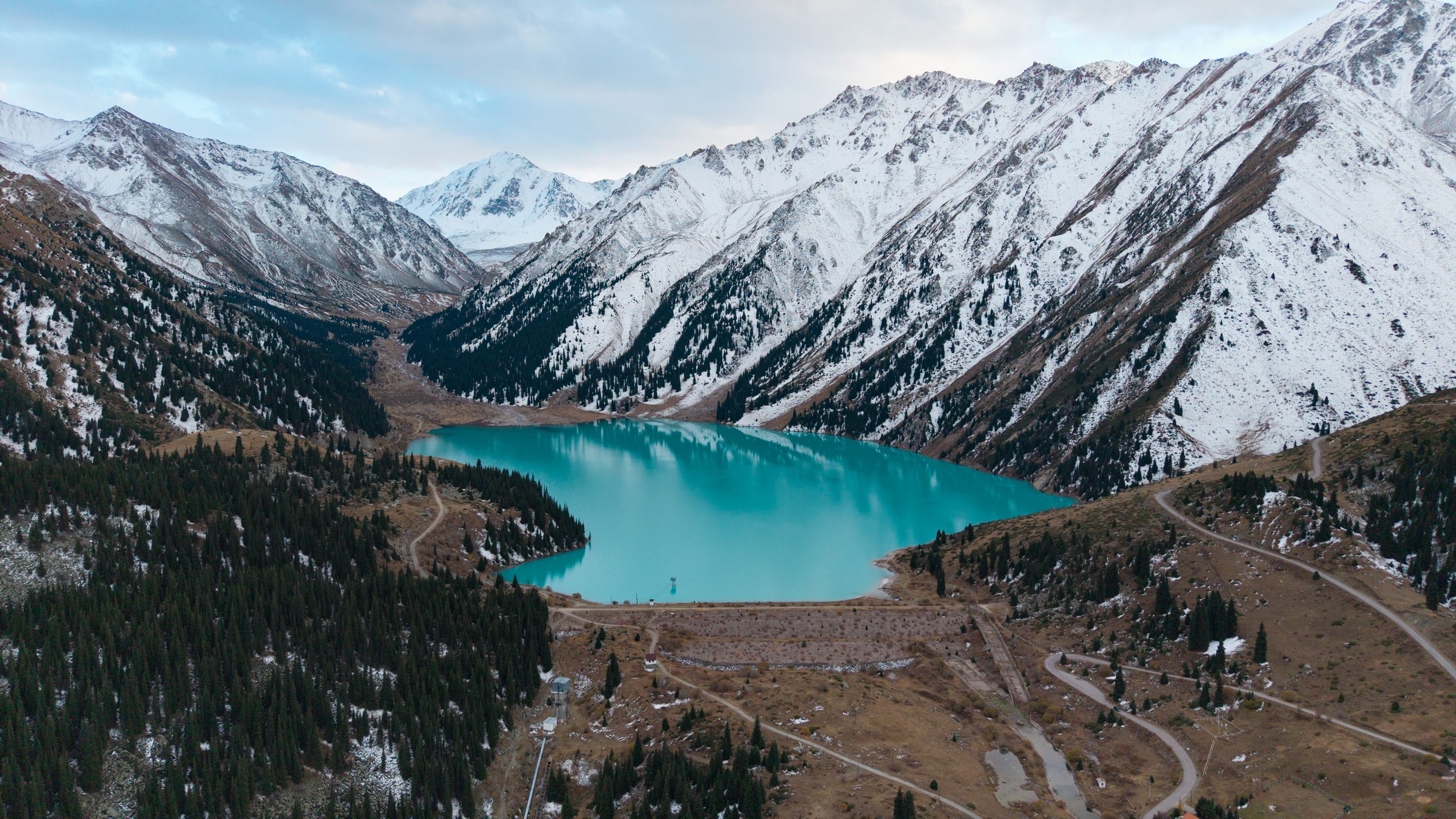 Aerial view of turquoise Big Almaty Lake surrounded by snow-covered Tian Shan peaks