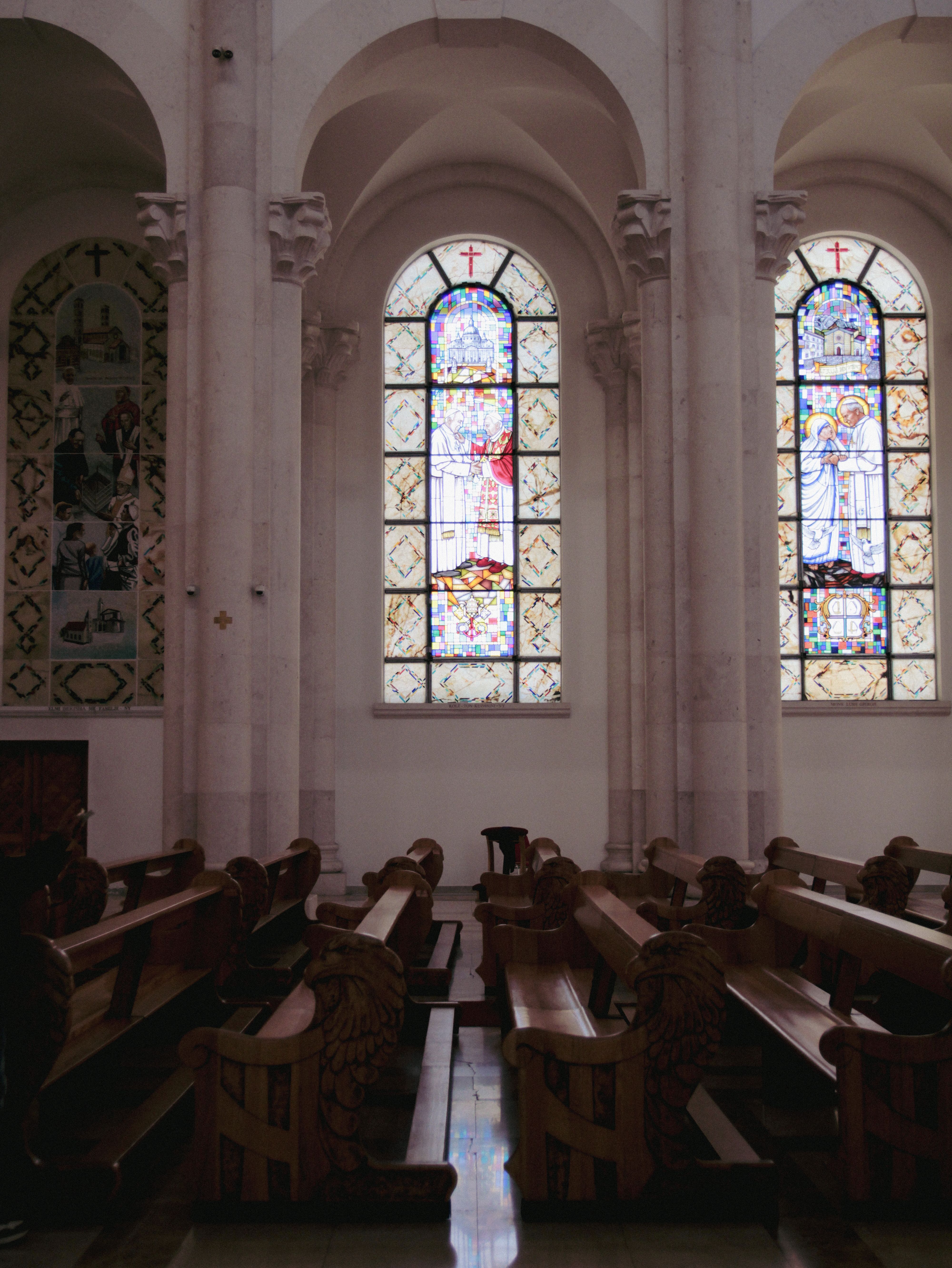 Beautiful stained glass windows illuminate a serene church interior with wooden pews.