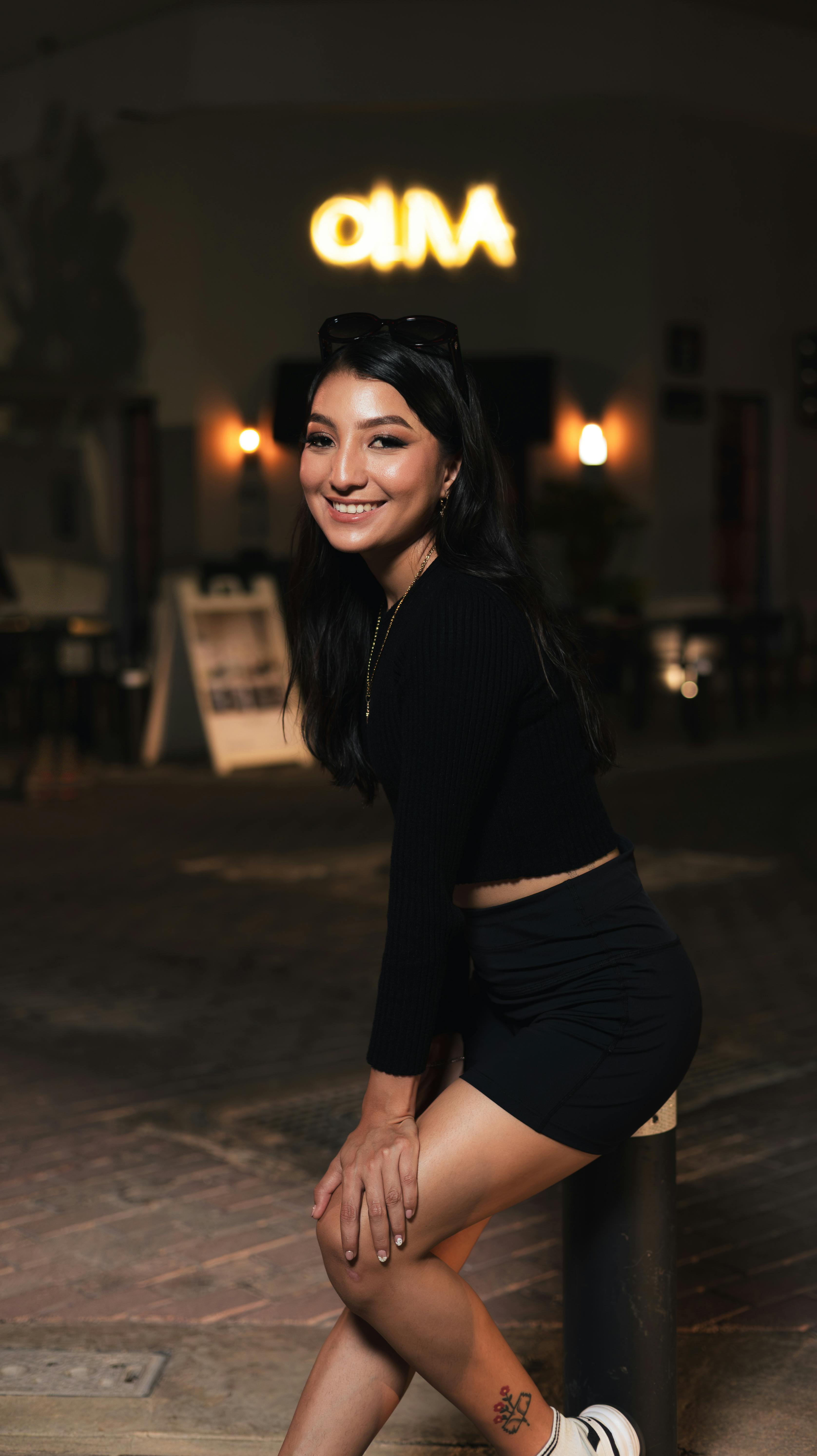 Free A young woman poses confidently at night, wearing a black outfit and smiling warmly. Stock Photo