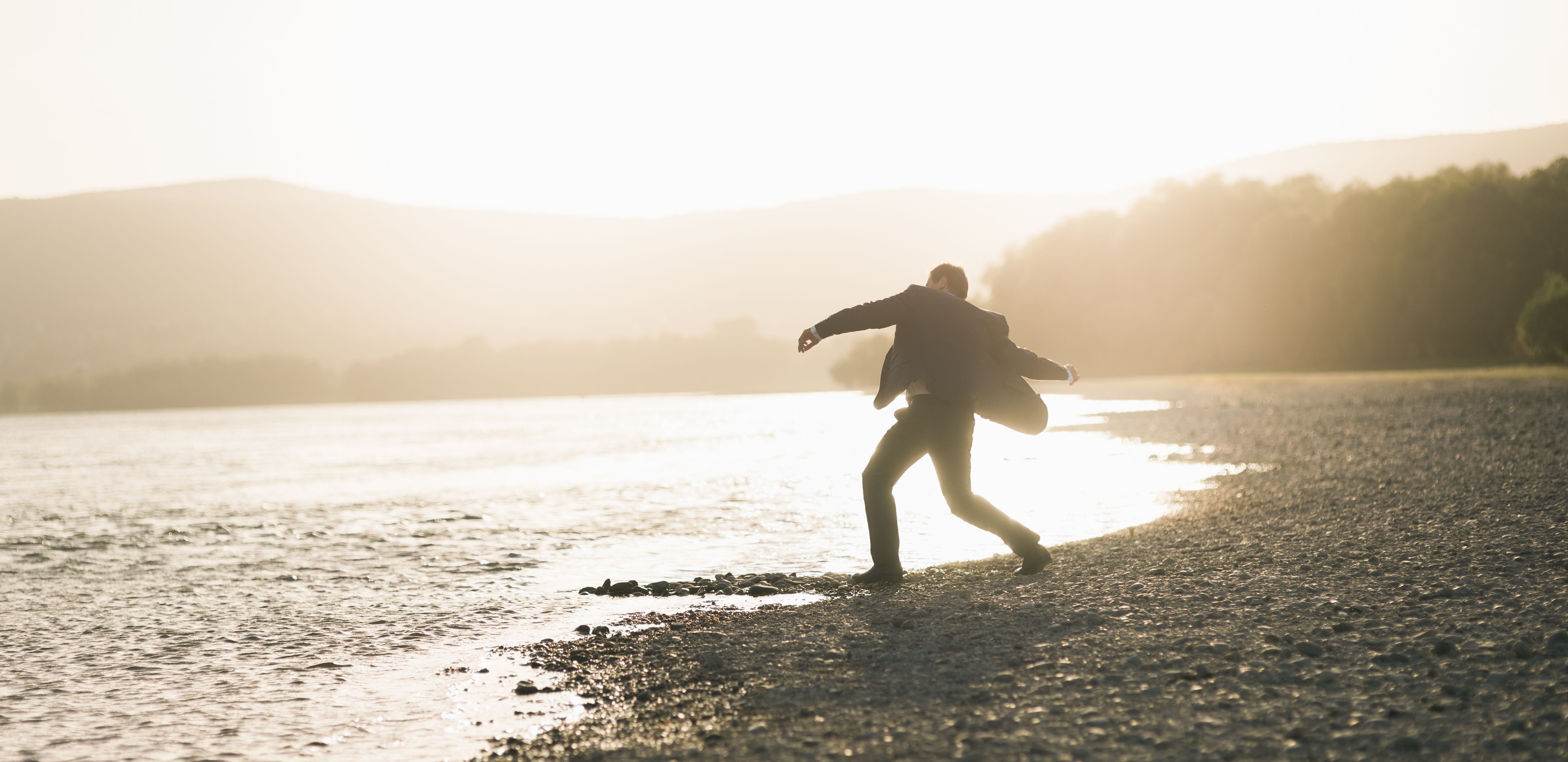Silhouette of Man Skipping Rocks at Sunset by Lake · Free Stock Photo