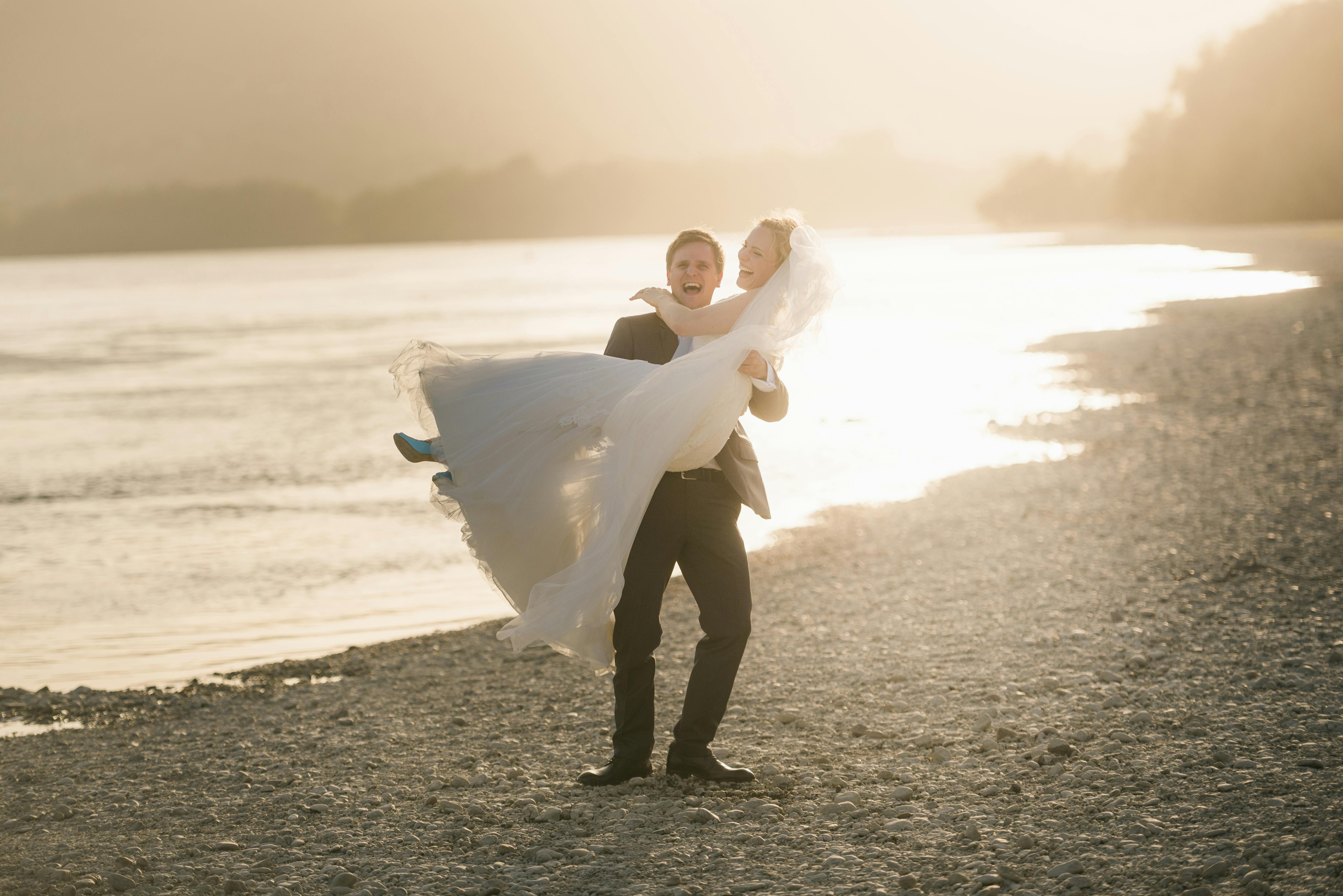 Bride and groom celebrate their wedding day on a beach at sunset, embracing love and joy.