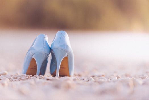 Stylish blue high heel shoes photographed on a tranquil pebble beach setting.