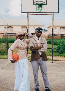 Stylish pair posing confidently under basketball hoop, embracing urban fashion